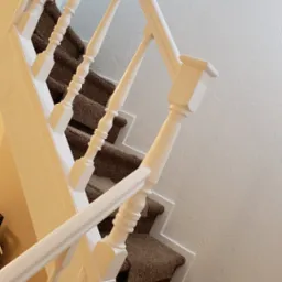 Bieg schod&oacute;w z brązową wykładziną i białymi, malowanymi balustradami oraz ozdobnymi słupkami, widok z dołu.