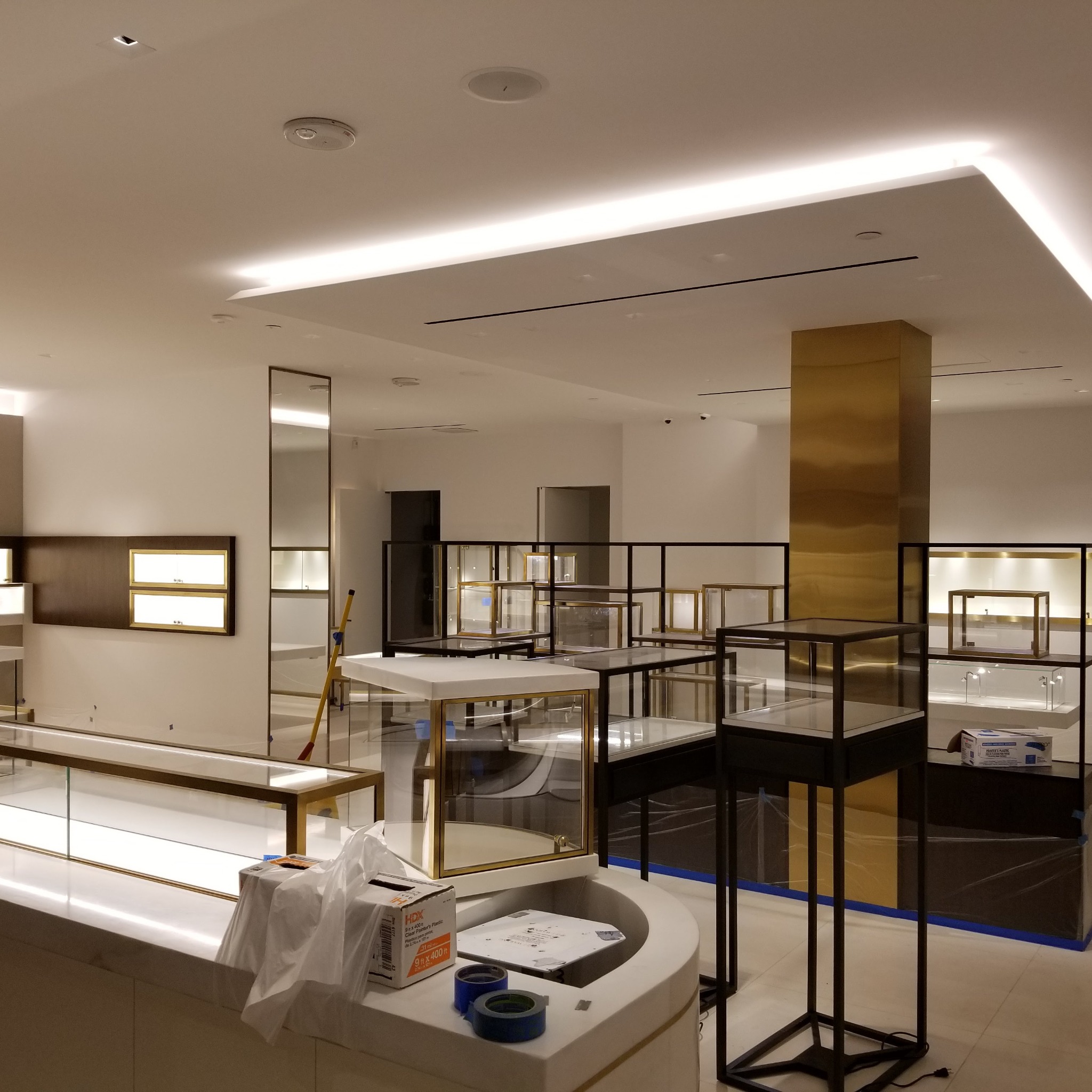 Wnętrze sklepu jubilerskiego w trakcie wyposażania, widoczne szklane gabloty z oświetleniem, materiały budowlane i zabezpieczenia na podłodze.