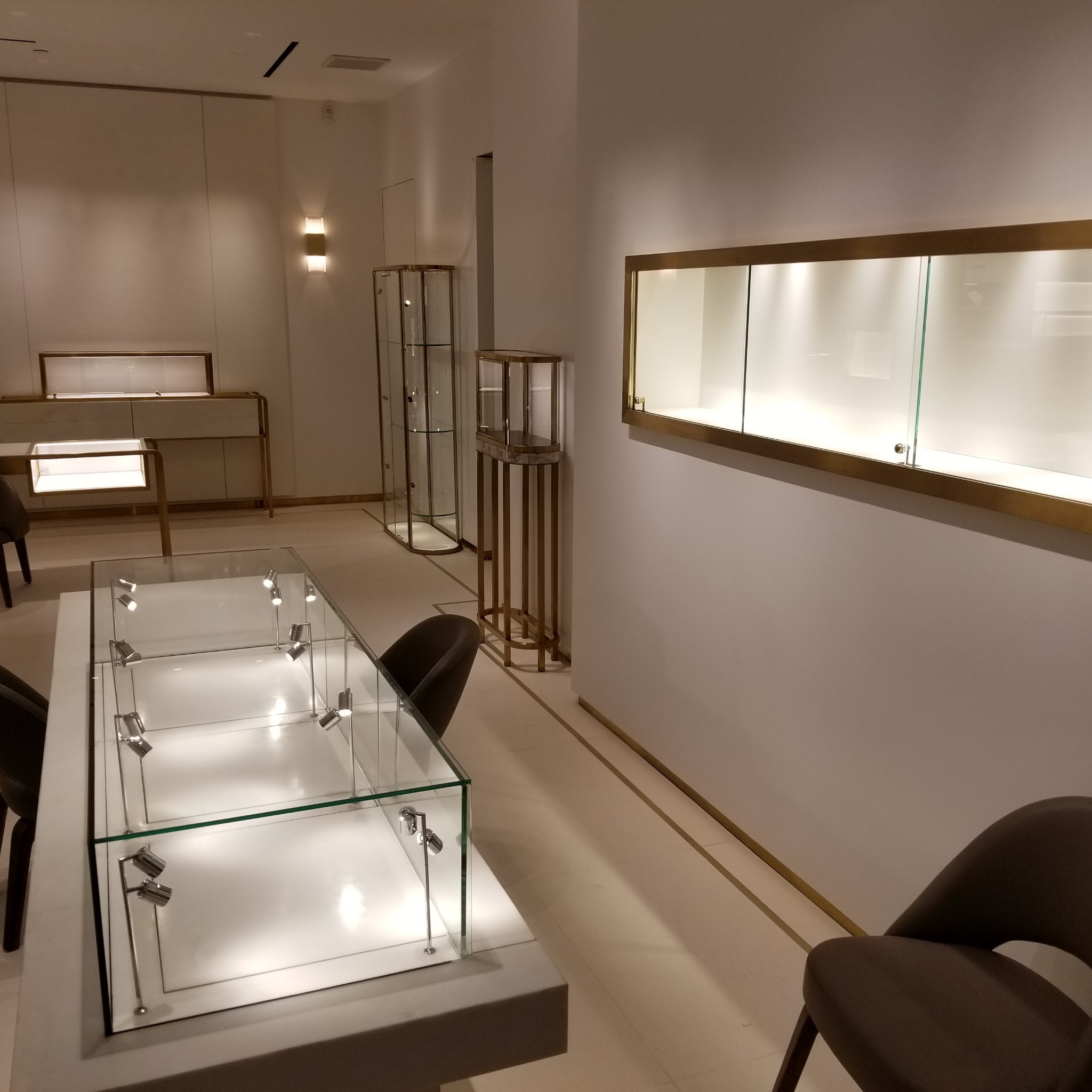 Wnętrze sklepu z ekspozycją biżuterii w szklanych gablotach z oświetleniem punktowym, minimalistyczny design z elementami w kolorze złotym.