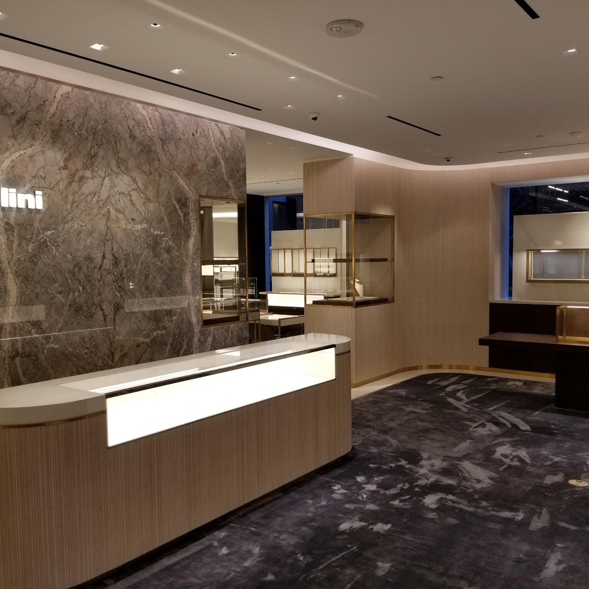 Wnętrze sklepu z luksusową ladą recepcyjną z podświetleniem LED, marmurową ścianą z logo i witrynami ekspozycyjnymi.