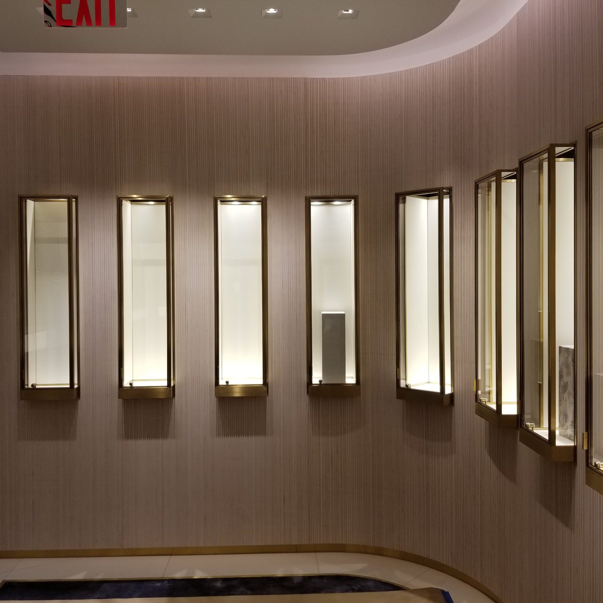 Wbudowane, podświetlane gabloty z brązowymi ramami na ścianie z teksturowaną tapetą, widoczny fragment podłogi z ciemnym wzorem.