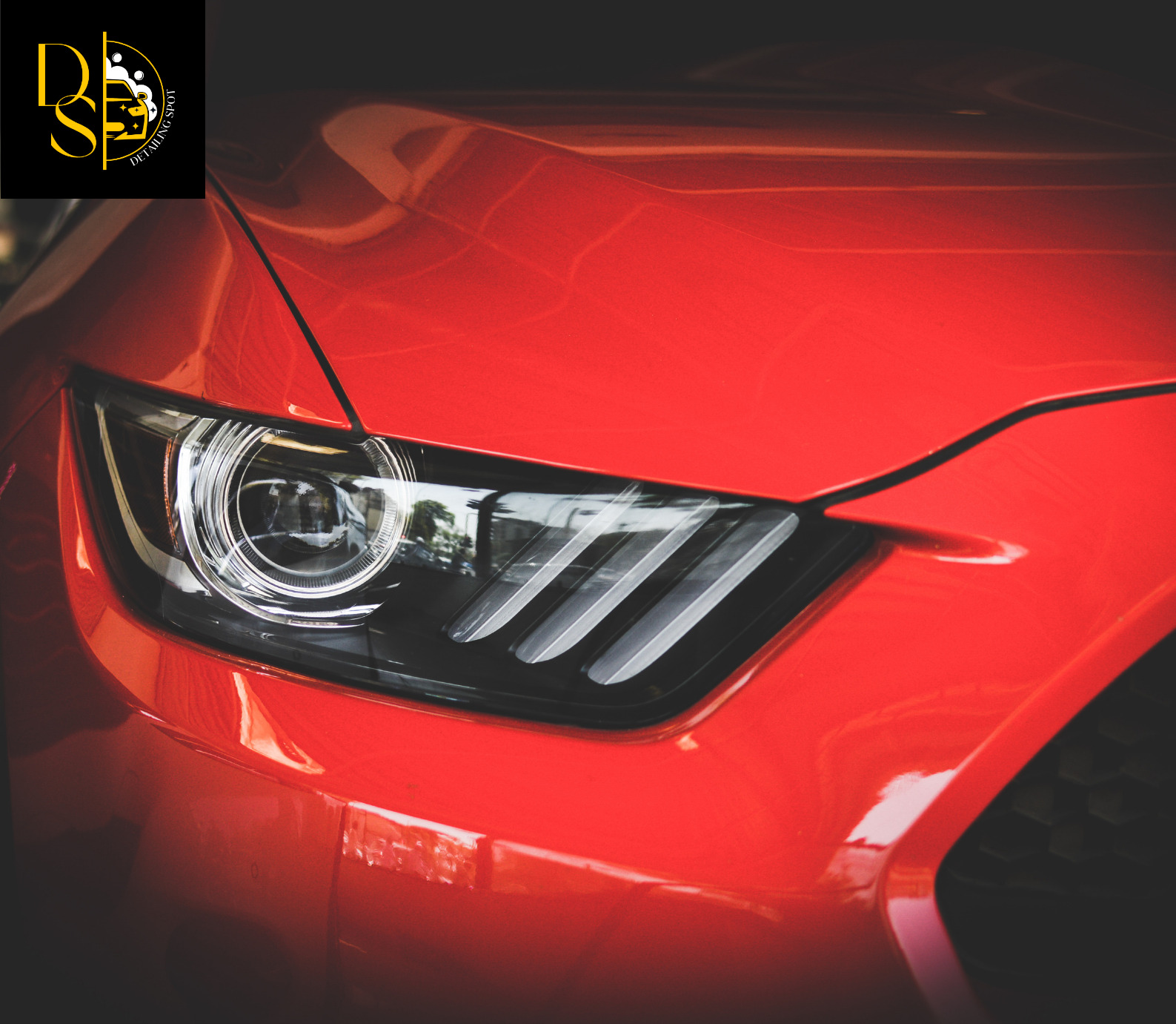 Czerwony samochód z widocznym reflektorem i logo firmy detailingowej w lewym górnym rogu.