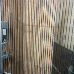 Kabina prysznicowa z wykończeniem ścian z drewnianych paneli pionowych, widoczna słuchawka prysznicowa i półka z kosmetykami.