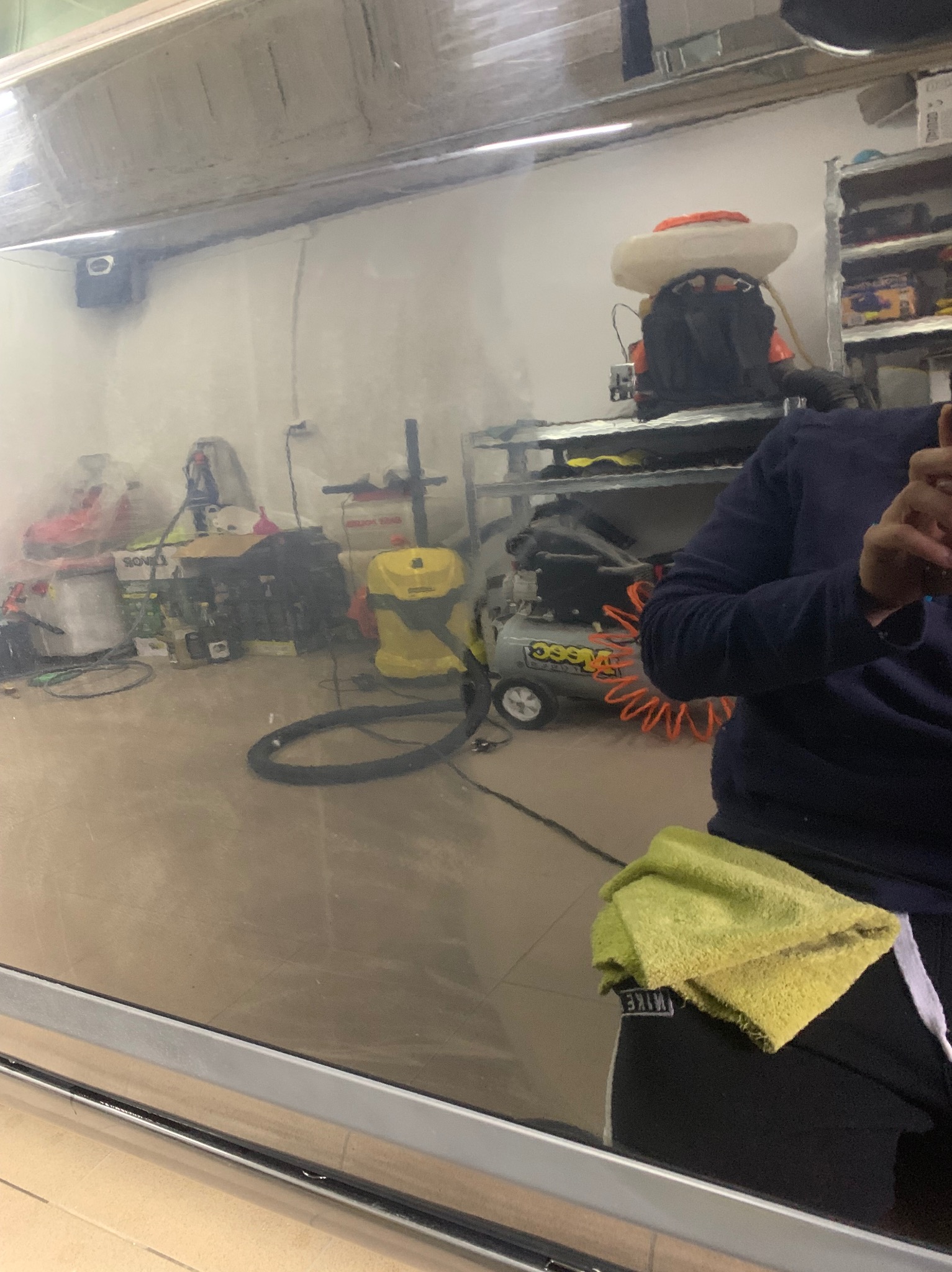 Odbicie warsztatu w świeżo wypolerowanej karoserii samochodu, widoczny kompresor, odkurzacz i osoba z żółtą ściereczką.