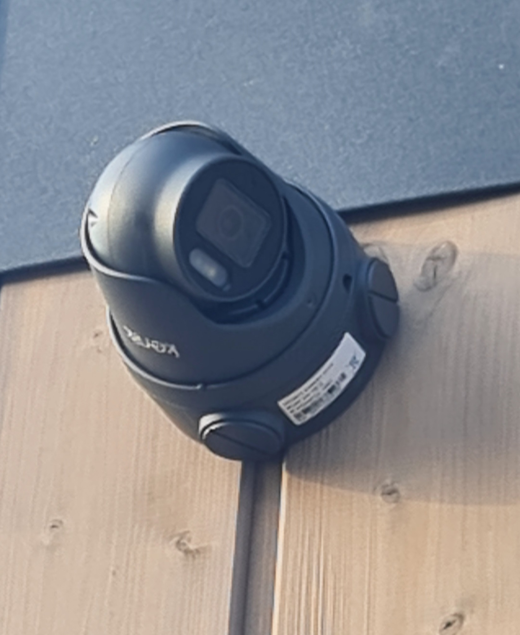 Kamera obrotowa monitoringu zewnętrznego, zamontowana na drewnianej elewacji budynku, widoczna tabliczka znamionowa z danymi technicznymi.