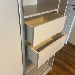 Bana Meble Rafał Korzeniowski - Jasna szafa z szufladami na wymiar, widoczne dwie wysunięte szuflady. Realizacja z Kalwarii Zebrzydowskiej. Minimalistyczny design, drewniana podłoga.