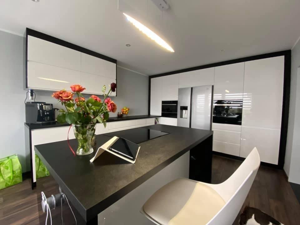 Nowoczesna kuchnia z wyspą i białymi szafkami z czarnymi obramowaniami w Kalwarii Zebrzydowskiej. Na blacie stoi wazon z różami i tablet.