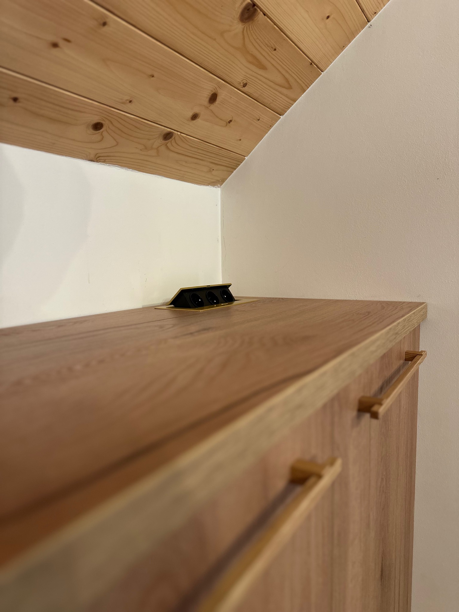 Fragment szafki z blatem z drewna z wbudowanym gniazdkiem elektrycznym, widok z dołu, drewniana podsufitka. Detal wykończenia wnętrza.