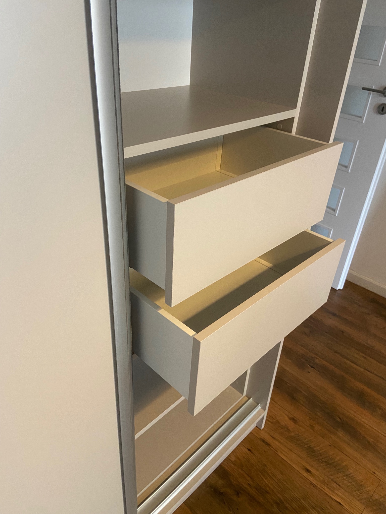 Jasna szafa z szufladami na wymiar, widoczne dwie wysunięte szuflady. Realizacja z Kalwarii Zebrzydowskiej. Minimalistyczny design, drewniana podłoga.