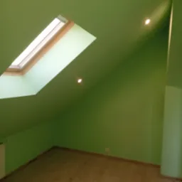 Poddasze po malowaniu na zielono z oknem dachowym i panelami podłogowymi, widoczne punkty świetlne w suficie.