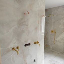Art-dom - Montaż złotej armatury łazienkowej na ścianie z płytek imitujących marmur, widoczne przygotowane punkty instalacyjne