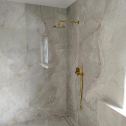 Art-dom - Wykończona kabina prysznicowa z marmurowymi płytkami, złotą armaturą i odpływem liniowym w podłodze.