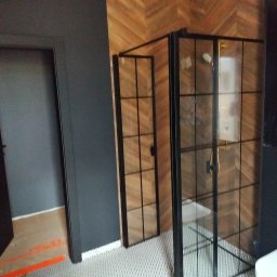 Art-dom - Nowoczesna kabina prysznicowa z czarnymi ramami i złotymi uchwytami w łazience w Pile, z drewnianą ścianą ułożoną w jodełkę i białą mozaikową podłogą.