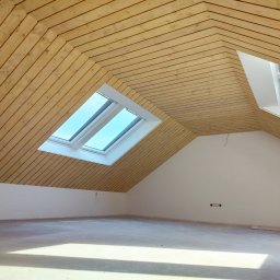 Art-dom - Poddasze z drewnianą boazerią na skośnym suficie i dwoma oknami dachowymi, ściany pomalowane na biało, surowa betonowa podłoga, widoczne gniazdka elektryczne.