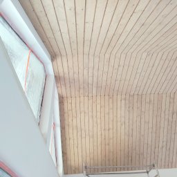 Art-dom - Drewniana boazeria na skośnym suficie z oknem dachowym w trakcie montażu, zabezpieczonym folią. Fragment drabiny malarskiej widoczny w rogu.