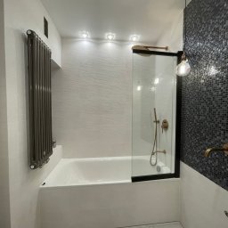 Oliwia Domagalska - Nowoczesna łazienka z wanną obudowaną płytkami, szklanym parawanem nawannowym z czarną ramą, grzejnikiem drabinkowym w kolorze grafitowym, mozaiką na ścianie i marmurową podłogą.