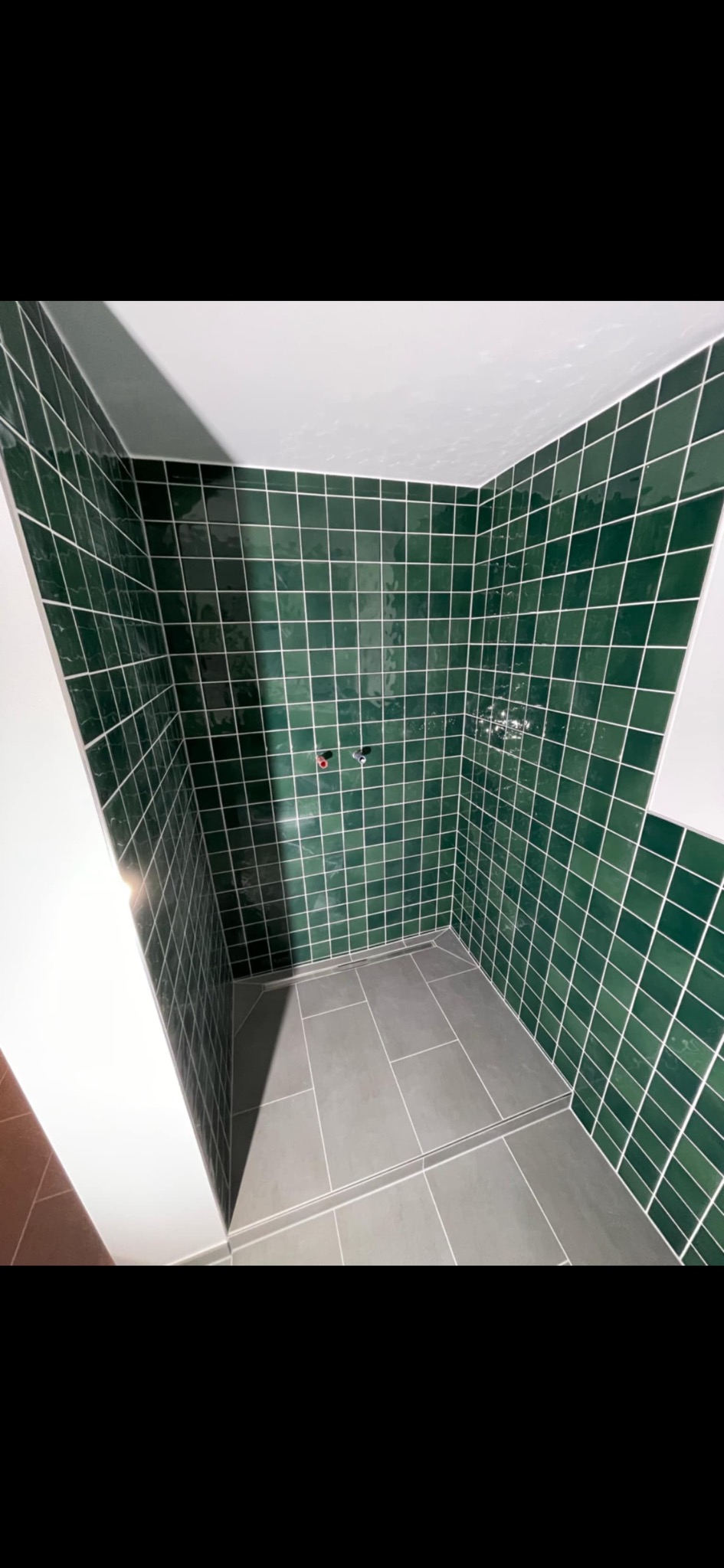 Kabina prysznicowa z zielonymi, kwadratowymi płytkami i szarą podłogą. Widoczne białe fugi i minimalistyczny odpływ liniowy.