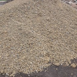 ARTUR JANCZAR AMJ-TRANS - Kupa żwiru o nieregularnej powierzchni, z widocznymi kamieniami różnej wielkości, na tle ziemi. Ujęcie z bliska, ukazujące strukturę materiału.