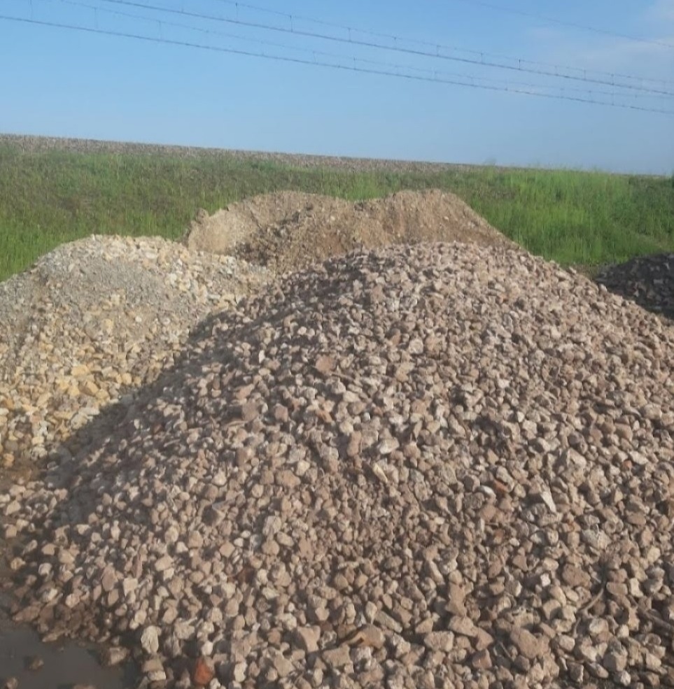 Kupa żwiru o nieregularnych kształtach i zróżnicowanej kolorystyce, na tle zieleni i błękitnego nieba. Widoczne drobne kamienie i frakcje.