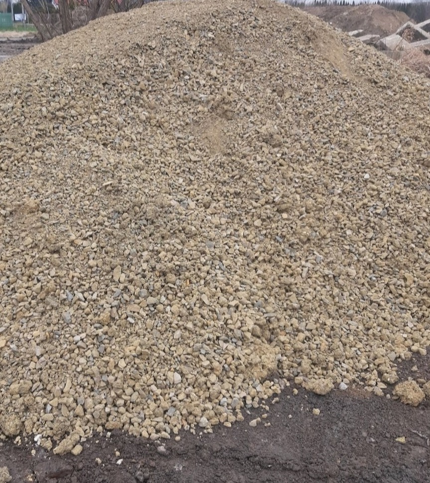 Kupa żwiru o nieregularnej powierzchni, z widocznymi kamieniami różnej wielkości, na tle ziemi. Ujęcie z bliska, ukazujące strukturę materiału.