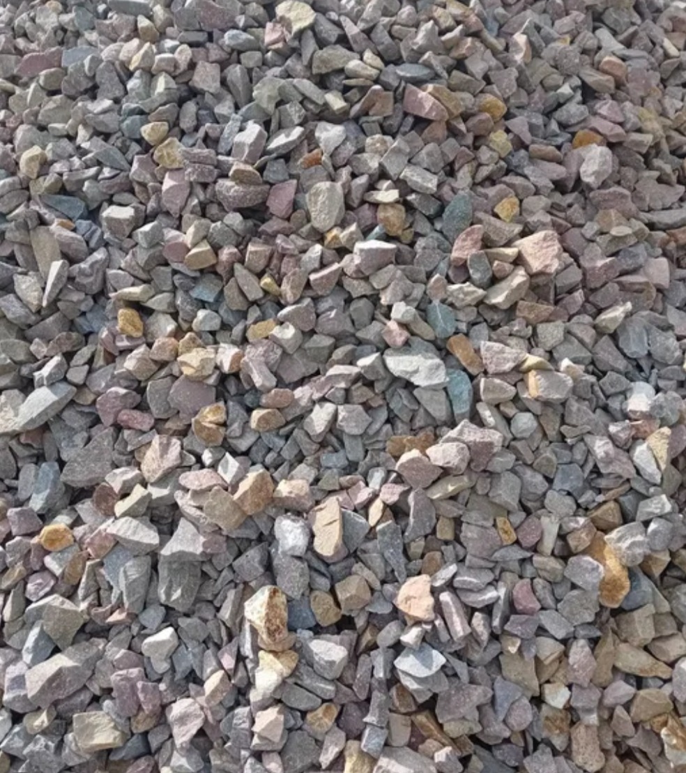 Kadr z bliska na pryzmę żwiru o nieregularnych kształtach i zróżnicowanej kolorystyce, od szarości po beże i delikatne róże. Widoczne drobne detale faktury kamieni.