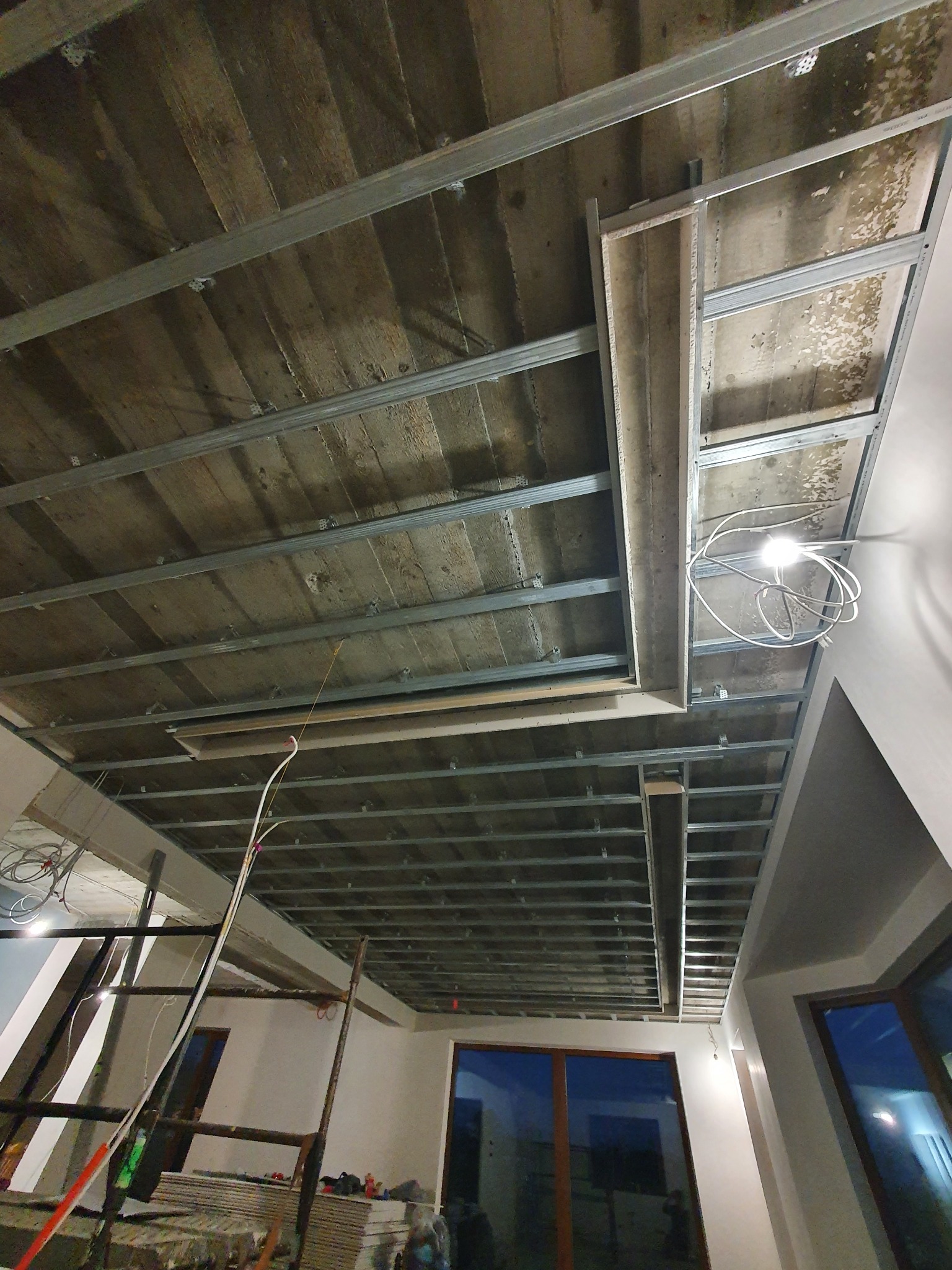 Sufit z zamontowaną metalową konstrukcją pod płyty gipsowo-kartonowe, widok z dołu, z widocznymi elementami oświetlenia i fragmentami ścian.