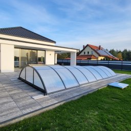 BudWare Roman Yevheichuk - Zadaszenie basenowe z poliwęglanu na tarasie z szarych płyt betonowych przy nowoczesnym domu z białymi ścianami i czarnym dachem.