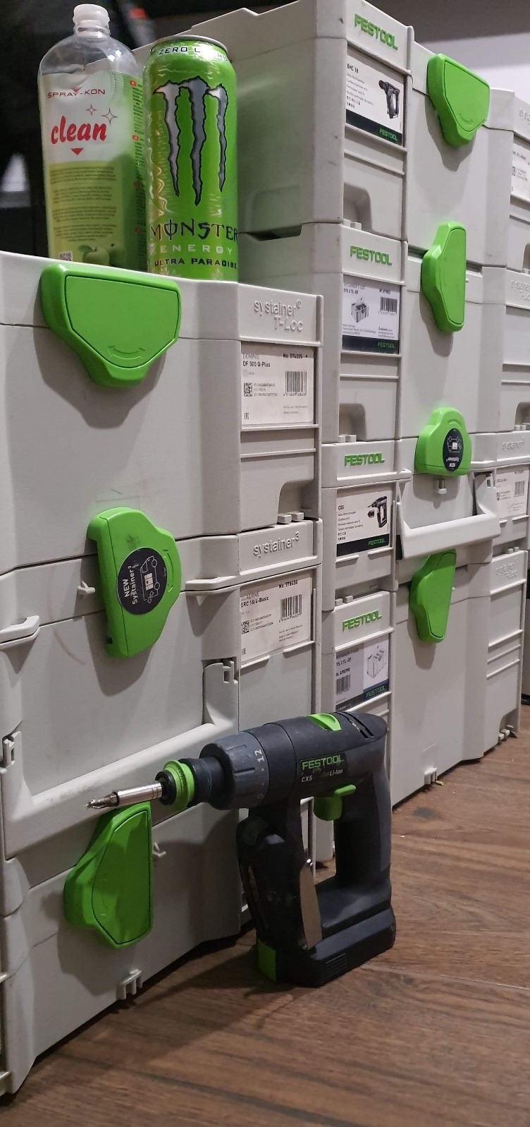 Wiertarko-wkrętarka Festool CXS na tle skrzynek Systainer, z puszką Monster Energy i płynem czyszczącym. Widok na narzędzie i system przechowywania.