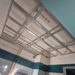 Usługi remontowo-budowlane Paweł Biel - Stelaż sufitu podwieszanego z płyt karton-gips w łazience w trakcie montażu. Widoczne profile metalowe, częściowo zamontowane płyty i instalacje.