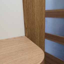 KEM Marcin Wielicki - Zaokrąglony narożnik jasnego, drewnianego blatu przylegający do białej ściany, z widoczną ramą szklanych drzwi w tle.