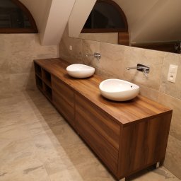 KEM Marcin Wielicki - Drewniana szafka łazienkowa z dwiema owalnymi umywalkami nablatowymi, chromowanymi bateriami i lustrem w skosie poddasza, wykończona płytkami w beżowym odcieniu.