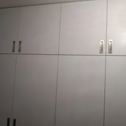 Szara zabudowa meblowa z minimalistycznymi, podłużnymi uchwytami, składająca się z szafek górnych i dolnych, o matowym wykończeniu.