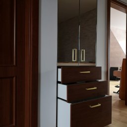 KEM Marcin Wielicki - Wbudowana szafa z lustrzanymi drzwiami i szufladami z ciemnego drewna z złotymi uchwytami; jedna szuflada jest otwarta, ukazując białe wnętrze.