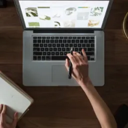 Widok z góry na biurko z laptopem wyświetlającym galerię zdjęć, otwarty kalendarz na wrzesień, kubek kawy, roślina doniczkowa i złota lampa, ukazujący proces pracy.