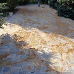 Finex-Bud - Świeżo ułożona szara kostka brukowa z piaskiem do wypełniania fug, widoczny pracownik w oddali i drzewa w tle.