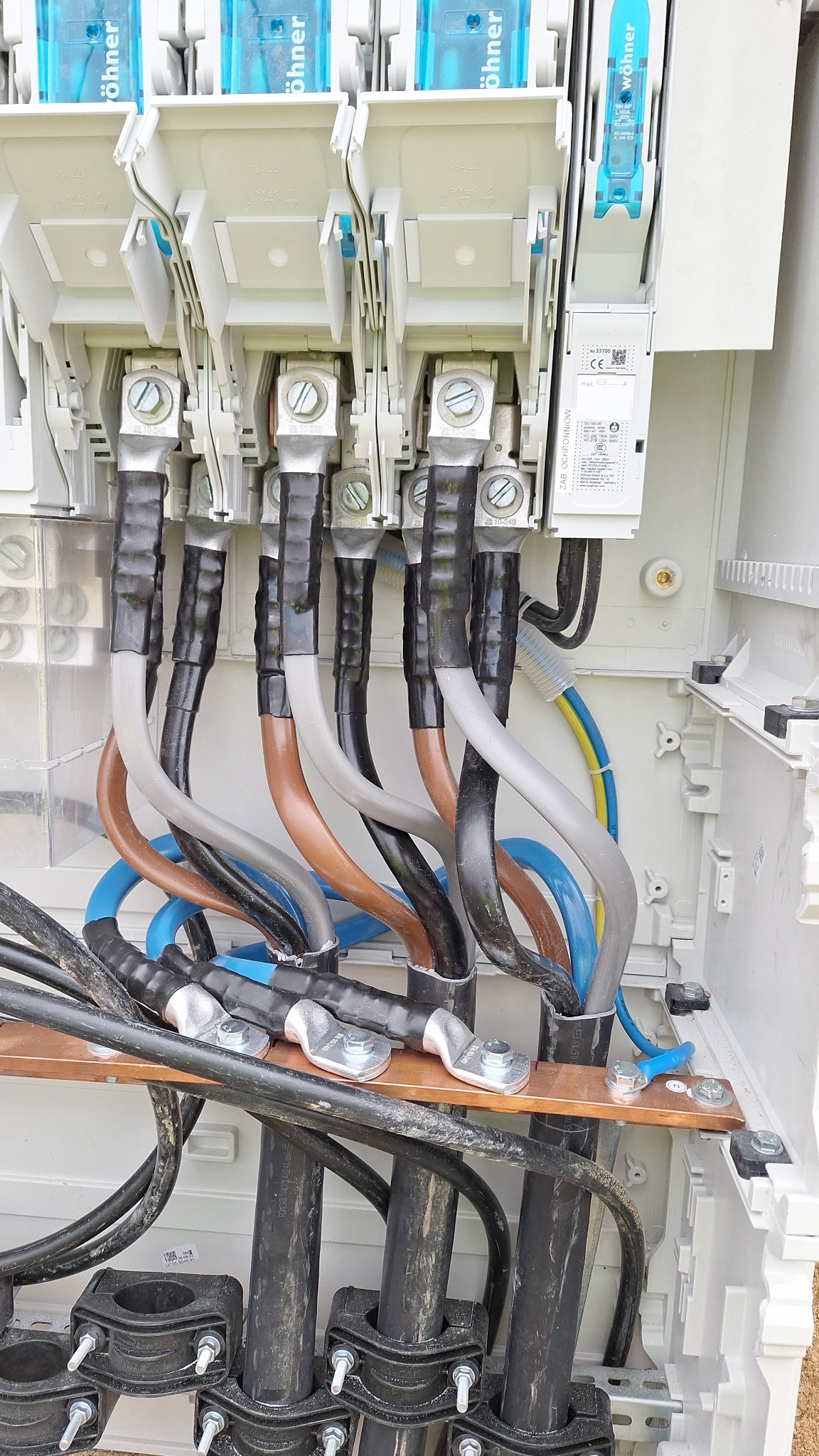 Rozdzielnica elektryczna z podłączonymi przewodami o różnych kolorach i przekrojach, widoczne zabezpieczenia Wöhner i listwa uziemiająca