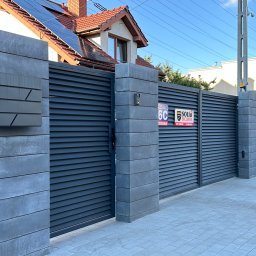 Kuźnia Stali ROKSANA ZADWORNA - Nowoczesna posesja z szarą, poziomą bramą lamelową, murowanymi słupkami z betonu architektonicznego i skrzynką na listy o geometrycznym designie.