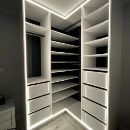 Furniture Mateusz Zuber - Biała, narożna szafa wnękowa z podświetleniem LED, widok z dołu, marmurowa podłoga, logo firmy w rogu.