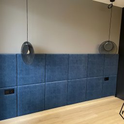 Furniture Mateusz Zuber - Niebieski, tapicerowany panel ścienny w sypialni z dwoma czarnymi gniazdkami elektrycznymi, oświetlony dwoma nowoczesnymi lampami wiszącymi z czarnymi kloszami, z szafą na ubrania w tle.