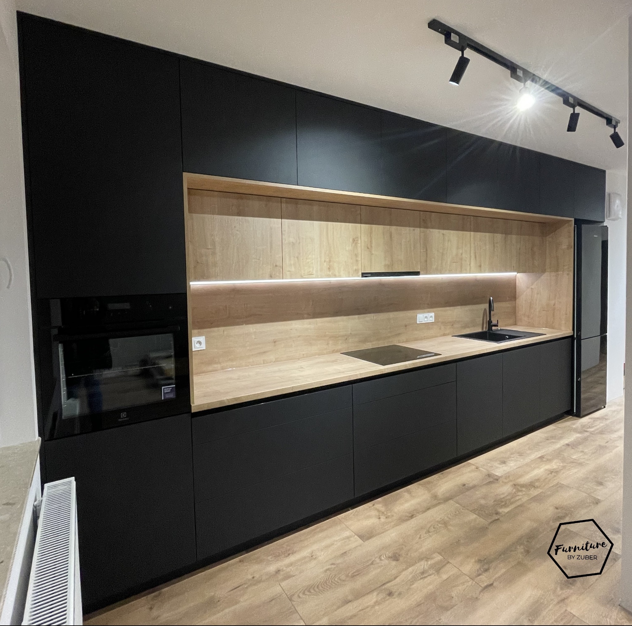 Nowoczesna kuchnia na wymiar z czarnymi frontami Forner Velvet Ultra Matt i drewnianym blatem Egger Dąb Hamilton naturalny, oświetlenie LED pod szafkami wiszącymi, widoczny zlew, płyta indukcyjna...