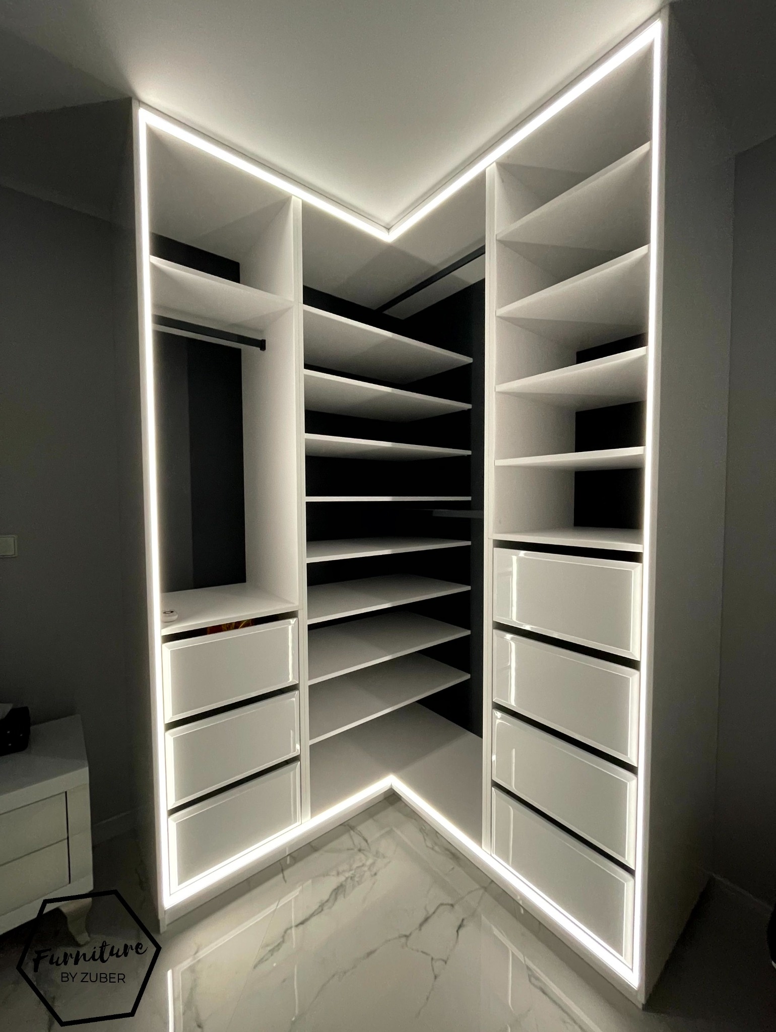 Biała, narożna szafa wnękowa z podświetleniem LED, widok z dołu, marmurowa podłoga, logo firmy w rogu.