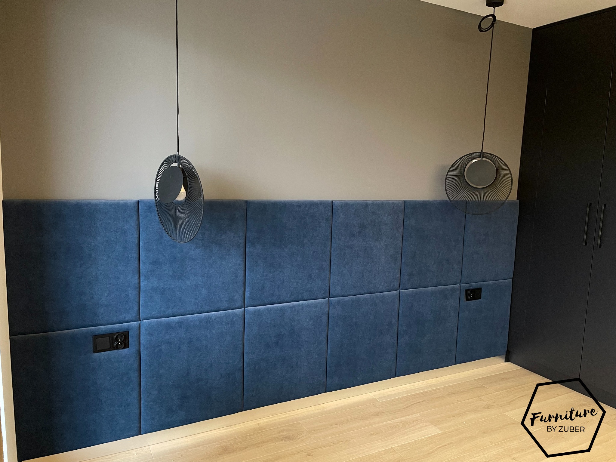 Niebieski, tapicerowany panel ścienny w sypialni z dwoma czarnymi gniazdkami elektrycznymi, oświetlony dwoma nowoczesnymi lampami wiszącymi z czarnymi kloszami, z szafą na ubrania w tle.