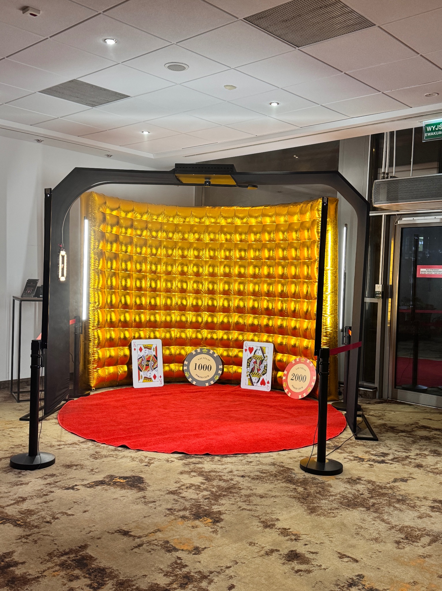 Fotobudka z motywem kasyna: złote tło z efektem pikseli, czerwony dywan, karty do gry (dama karo) i żetony pokerowe (1000 i 2000) na planie, oświetlenie LED po bokach.
