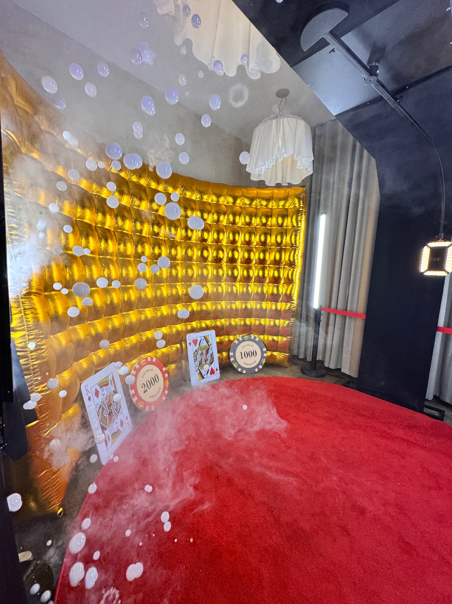 Scena z rekwizytami w stylu kasyna: złota ściana, karty do gry, żetony pokerowe i czerwony dywan, otoczone efektem mgły i bańkami.