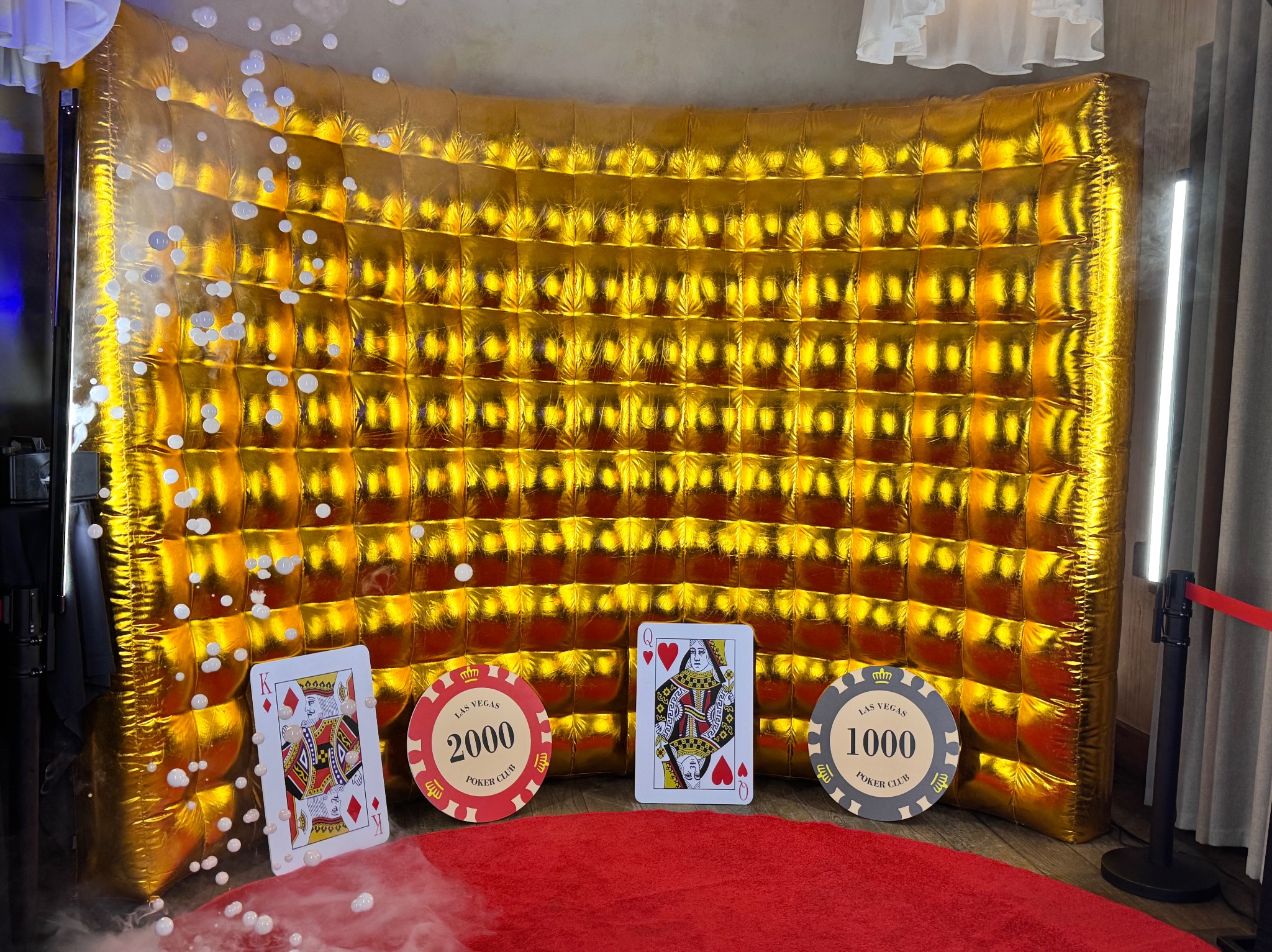 Inscenizacja z złotym, pikowanym tłem, kartami do gry (król i dama) oraz żetonami pokerowymi Las Vegas Poker Club na czerwonym dywanie, otoczona sztucznym dymem.