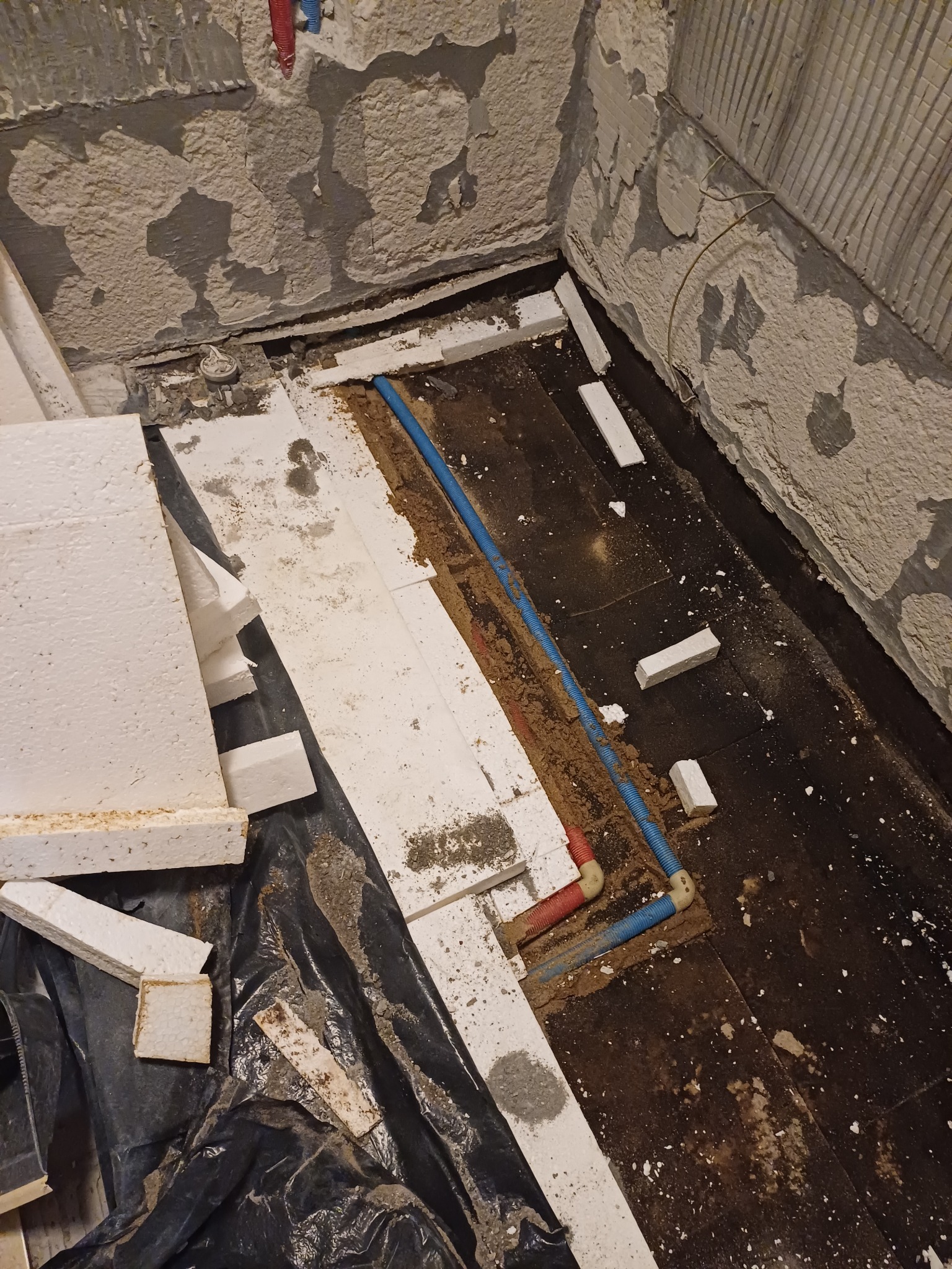 Przygotowanie podłoża: fragment podłogi w trakcie prac, widoczne rury instalacyjne, styropianowe płyty izolacyjne, nierówne ściany z resztkami starej zaprawy.