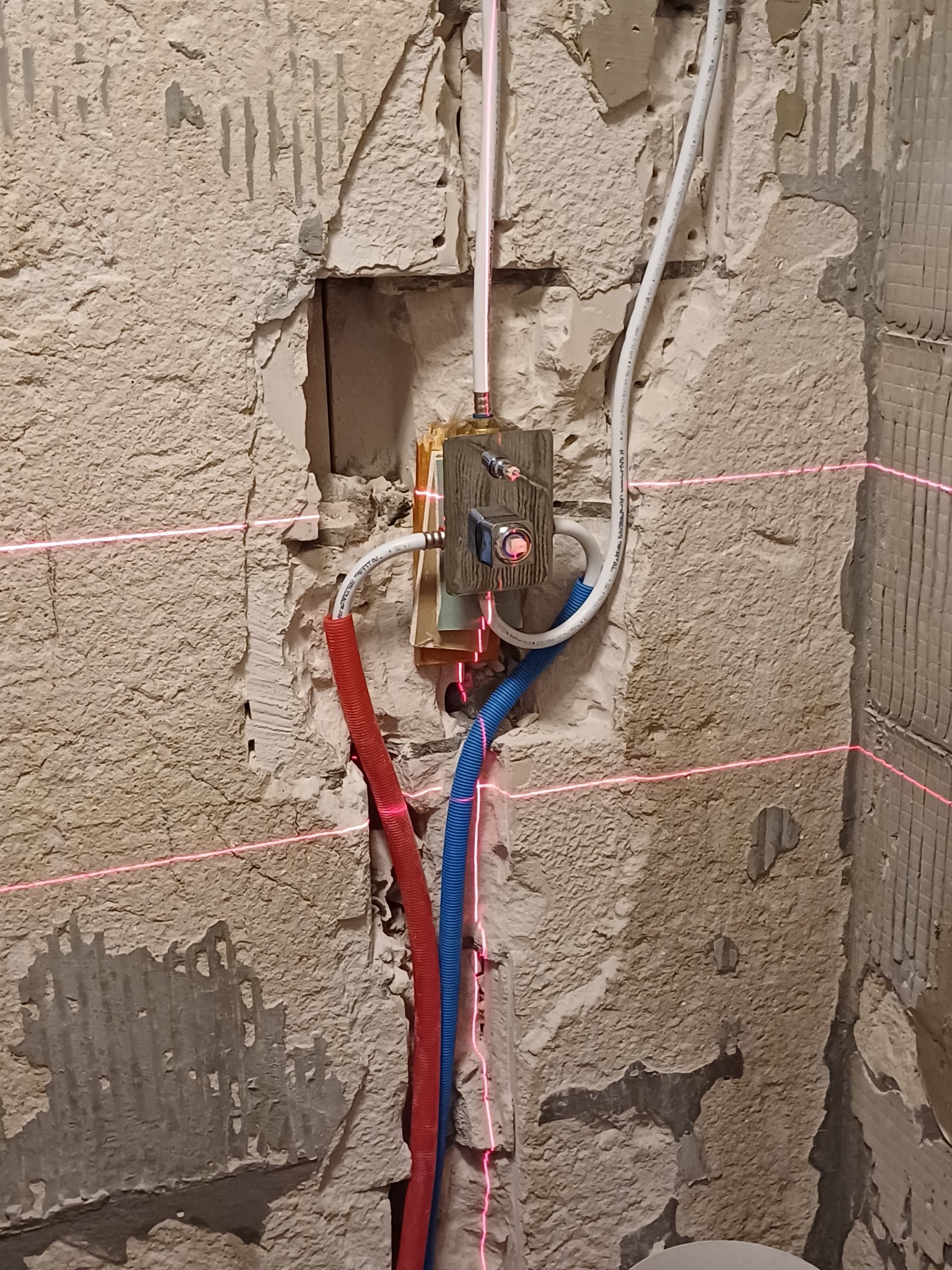 Przygotowanie ściany pod glazurę w Elblągu z użyciem poziomicy laserowej, widoczne rury instalacji wodnej w kolorze czerwonym i niebieskim oraz fragmenty starej glazury.