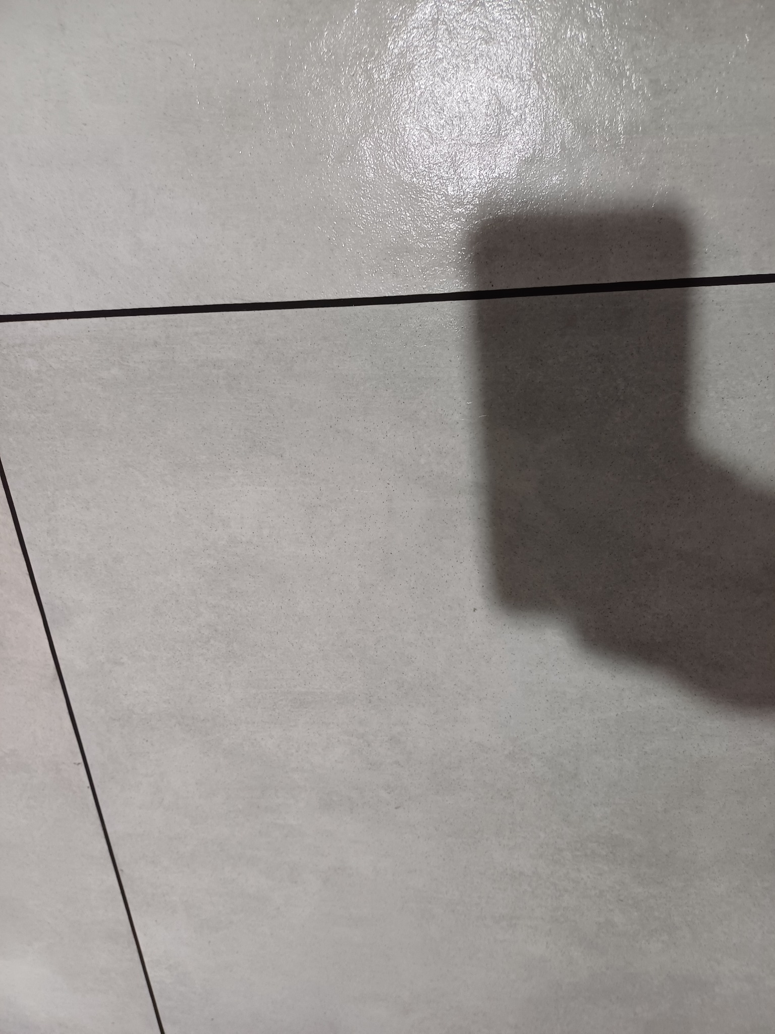 Jasnoszare płytki podłogowe z ciemnymi fugami i cieniem padającym z góry.