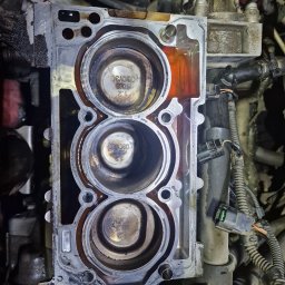 A.I.L Serwis - Otwarty blok silnika samochodowego z widocznymi trzema cylindrami, ślady oleju i nagaru, fragment instalacji elektrycznej w tle.