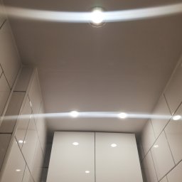 A.I.L Serwis - Sufit podwieszany z oświetleniem LED w łazience, białe płytki na ścianach i szafka z połyskiem.